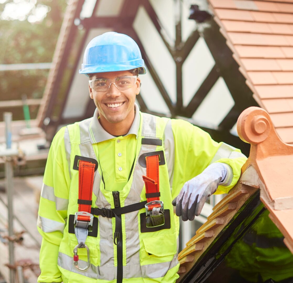 Construction worker smiling on rooftop in safety gear.